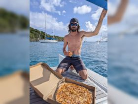 A man enjoys a slice of pizza on the deck of a boat, surrounded by beautiful ocean views — a perfect moment for relaxation and indulgence on the water.