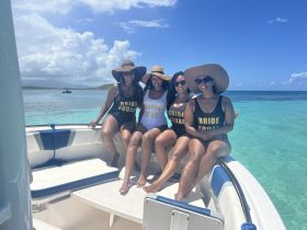 A fun group of friends celebrates a bridal party on a boat, showcasing their 'Bride Squad' swimsuits against a stunning turquoise backdrop — perfect for bachelorette adventures.