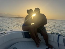 A couple shares a romantic kiss on the bow of a boat during sunset, creating a perfect backdrop for memorable moments on the water.