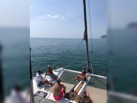 A lively group enjoys a relaxing day on a catamaran, soaking up the sun and sipping drinks while surrounded by tranquil waters.