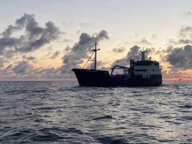 A fishing vessel named 'OCEARCH' navigates the ocean at sunset, showcasing the serene beauty of maritime life.