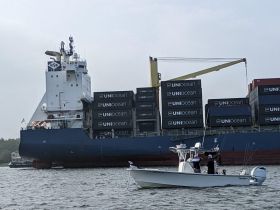 A small fishing boat navigates alongside a large cargo ship, showcasing the contrast between recreational and commercial boating on the water.