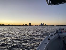 A serene sunset view from the deck of a boat, showcasing a beautiful city skyline reflected in the water — perfect for evening cruises.