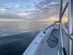 A serene view of a boat's hull against a calm sea at sunrise, showcasing the tranquility of early morning boating.