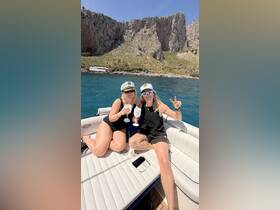Two friends celebrate on a boat with cocktails, enjoying a sunny day surrounded by stunning cliffs — perfect for memorable outings and gatherings on the water.