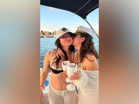 Two friends share a joyful moment on a boat, celebrating with cocktails and wearing captain hats — perfect for a fun day on the water.