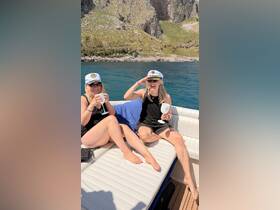 Two friends enjoy cocktails on a sunny day aboard a boat, celebrating their time on the water with smiles and laughter.