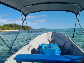 A serene view from the bow of a boat, showcasing clear turquoise waters and a lush island backdrop — perfect for exploring coastal destinations.