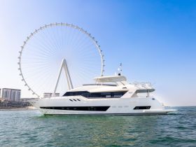 A stunning yacht glides through the water with a prominent Ferris wheel in the background, showcasing a perfect blend of luxury and leisure.