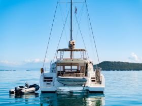 A stunning view of a catamaran from the back, anchored in calm waters, showcasing its sleek design against a clear blue sky.