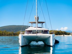 A stunning front view of a catamaran anchored in calm waters, surrounded by lush greenery and clear blue skies — perfect for serene sailing adventures.