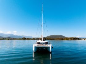 A stunning view of a catamaran anchored in calm waters, showcasing its sleek design against a backdrop of mountains and clear blue skies — perfect for serene sailing adventures.