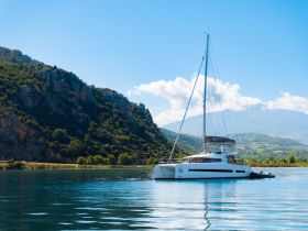 A stunning catamaran anchored in calm waters, surrounded by lush hills and clear blue skies, perfect for serene sailing adventures.