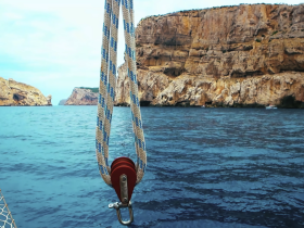 A close-up view of a sailboat's pulley system with stunning rocky cliffs in the background, showcasing the beauty of coastal sailing.