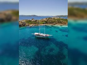 A stunning aerial view of a sailboat anchored in crystal-clear turquoise waters, surrounded by rocky landscapes — perfect for exploring coastal destinations.