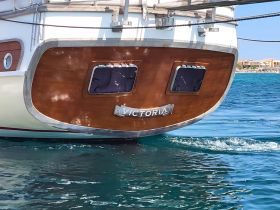 Close-up view of the back of a boat named 'Victoria' gliding through clear waters, showcasing its elegant design and craftsmanship.