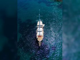A stunning aerial view of a yacht gliding through crystal-clear waters, showcasing its elegant design and the beauty of the surrounding seascape.
