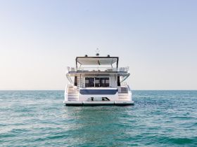 A stunning view of a modern yacht cruising through clear waters, showcasing its elegant design and spacious back deck.