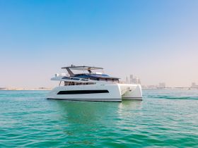 A stunning catamaran glides through clear turquoise waters, showcasing its sleek design against a backdrop of a vibrant skyline.