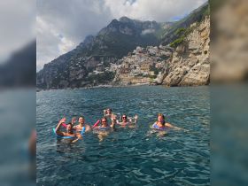 A lively group enjoys a refreshing swim in the crystal-clear waters of the Amalfi Coast, surrounded by stunning coastal scenery.