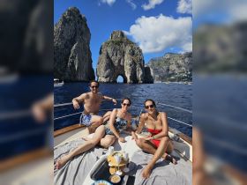 A group of friends relaxes on a boat near the iconic rock formations of Capri, enjoying snacks and drinks under the sun — a perfect day on the water.