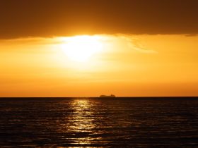 A serene sunset view over the ocean with a distant boat silhouetted against the vibrant orange sky, perfect for capturing the beauty of maritime landscapes.