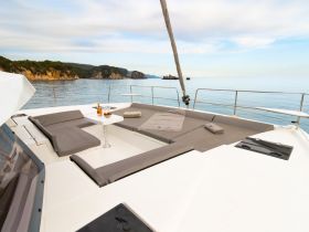 A serene view of the lounge area on a catamaran, featuring comfortable seating and a table, perfect for relaxing while enjoying the stunning coastal scenery.