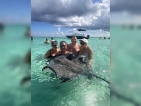 A group of friends interacts with a stingray in shallow turquoise waters, creating a memorable wildlife experience in a tropical paradise.