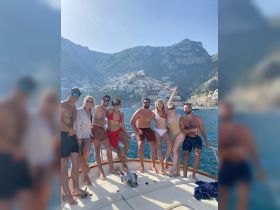 A lively group of friends celebrates aboard a boat with stunning coastal views, perfect for summer adventures and memorable outings on the water.