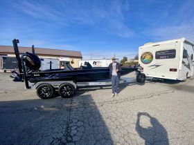 A sleek fishing boat is showcased on its trailer, with a person giving a thumbs up, ready for an adventure on the water.