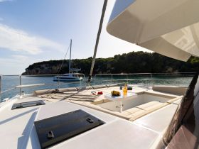 A beautifully set table on the deck of a catamaran, featuring drinks and fresh bananas, perfect for relaxing moments at sea.