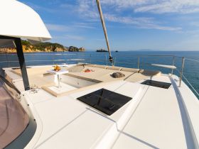 A serene view of the lounge area on a catamaran, featuring comfortable seating and a table, perfect for relaxation while enjoying the beautiful ocean scenery.