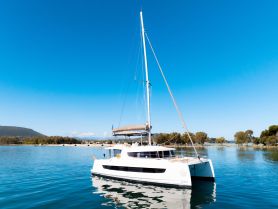 A stunning side view of a Bali catamaran docked in calm waters, surrounded by lush greenery and clear blue skies — perfect for serene sailing adventures.