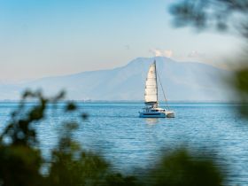 A serene view of a catamaran sailing across calm waters, framed by lush greenery and distant mountains, perfect for showcasing the beauty of sailing adventures.