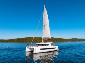 A stunning catamaran sails through calm waters, showcasing its sleek design against a backdrop of lush greenery — perfect for sailing adventures and island hopping.