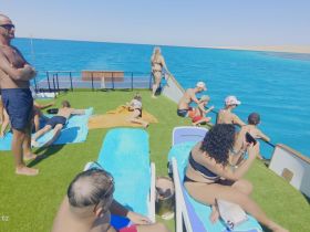 A lively group enjoys a sunny day on a boat, lounging and soaking up the sun while surrounded by stunning turquoise waters — perfect for family outings and relaxation.