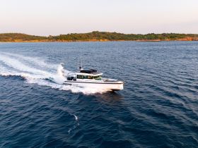 A sleek speedboat glides through the water, showcasing its elegant design against a scenic backdrop of lush greenery and calm waves.