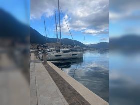 A serene view of a catamaran docked at a marina, surrounded by picturesque mountains and calm waters, perfect for a relaxing day by the sea.