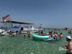 A lively group enjoys a fun day in the water with a boat tour backdrop, featuring swimming, floating, and socializing at a popular sandbar.