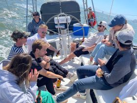 A lively group enjoys a day of sailing, sharing drinks and laughter on the deck — perfect for a fun outing on the water.