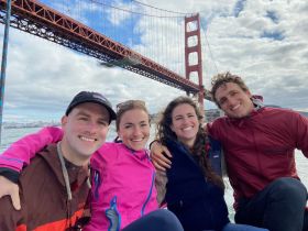 A cheerful group of friends poses for a photo with the iconic Golden Gate Bridge in the background, capturing a memorable moment on their boating adventure.