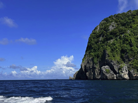A stunning view of a lush green coastline against a vibrant blue sky, showcasing the beauty of the ocean and nearby islands — perfect for nature lovers and adventure seekers.