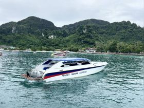 A sleek speedboat named 'Phuket Marine Express' glides through the tranquil waters, surrounded by lush green mountains, perfect for exploring the scenic beauty of Phuket.
