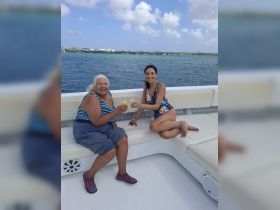 Two friends enjoy cocktails on a boat, celebrating their time together with stunning ocean views in the background.