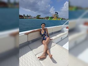 A woman relaxes on a boat, enjoying the sun and the vibrant scenery of a water park in the background — a perfect day for fun on the water.