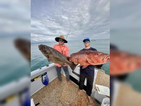 Two anglers proudly display their impressive catch aboard a fishing boat, showcasing a successful day on the water.