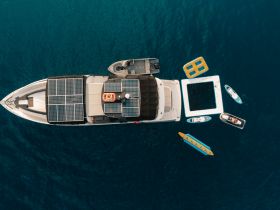 An aerial view of a luxurious boat equipped with solar panels, surrounded by various water toys including paddleboards and inflatables, perfect for a day of fun on the water.