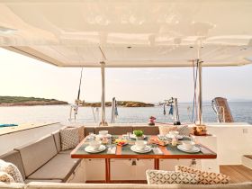 A beautifully arranged dining area inside a boat, featuring a table set for a meal with stunning views of the water and nearby island, perfect for enjoying meals while cruising.