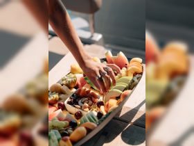 A hand reaches for a vibrant fruit platter filled with fresh fruits and nuts, perfect for enjoying on a boat trip. Ideal for catering or snack options while cruising.