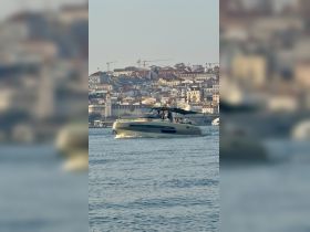 A stylish boat navigates through the water with a vibrant cityscape in the background, showcasing a lively day on the water.